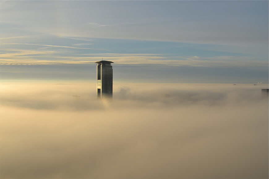 Skyscraper emerging from thick fog in a city at sunrise