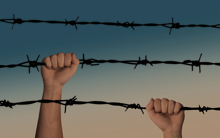 Hands gripping barbed wire fence against gradient sky background