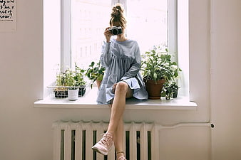 Woman with Camera Sitting on Window Sill with Plants