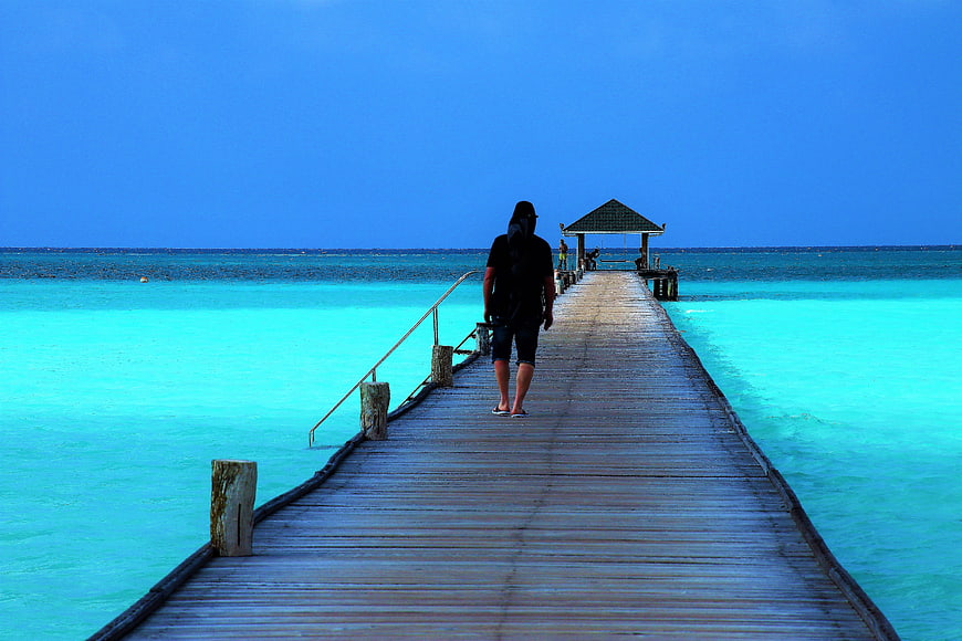 Man Walking On Wooden Pier In Maldives Turquoise Water