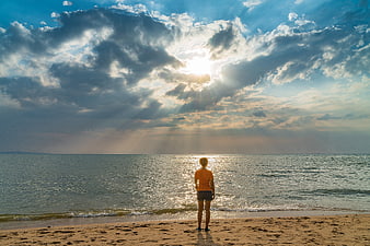 Woman standing on beach at sunset looking at ocean