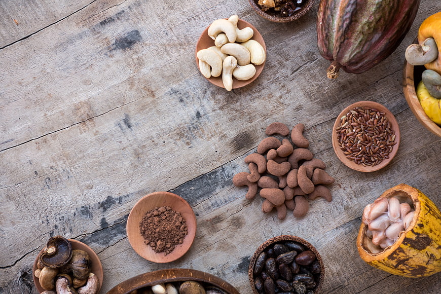 Top view of cocoa pods, cashews, and cacao nibs on rustic wood