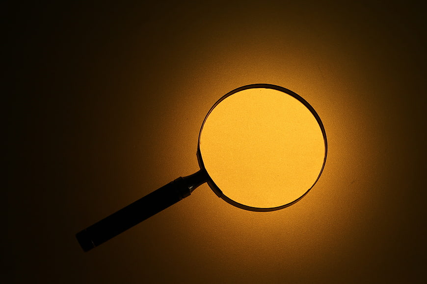 Magnifying glass silhouette against warm glowing amber background