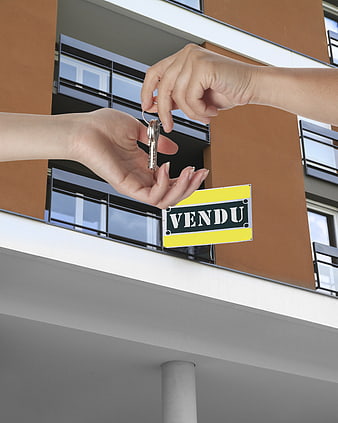 Handing over apartment keys with sold sign in front of modern building