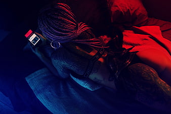 Tattooed Woman Lying on Bed Using Smartphone in Neon Light