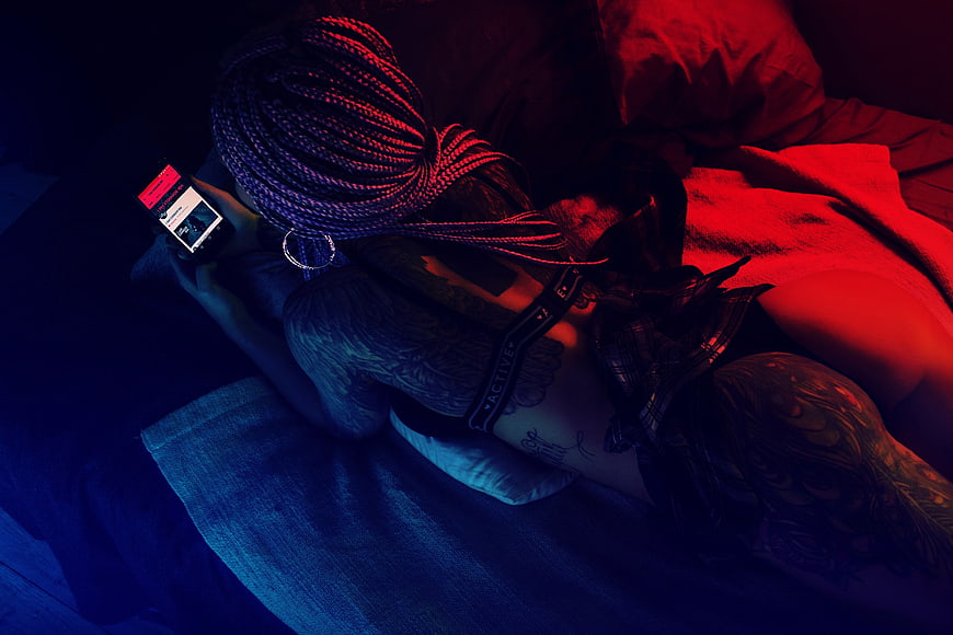 Tattooed Woman Lying on Bed Using Smartphone in Neon Light