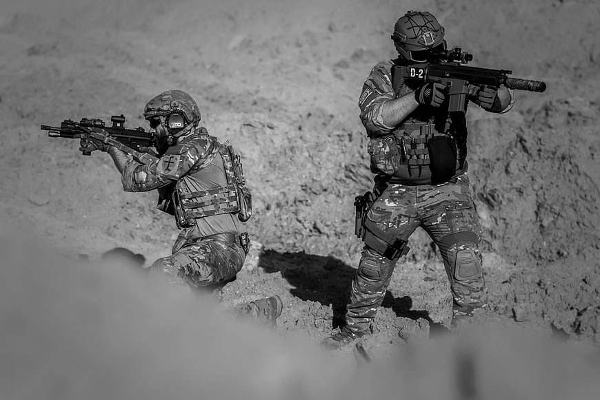 Two soldiers in tactical gear aiming rifles in black and white
