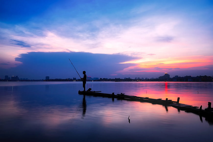 Silhouette of Man Fishing at Sunset on Calm Water