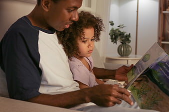 Father reading bedtime story to young daughter on couch