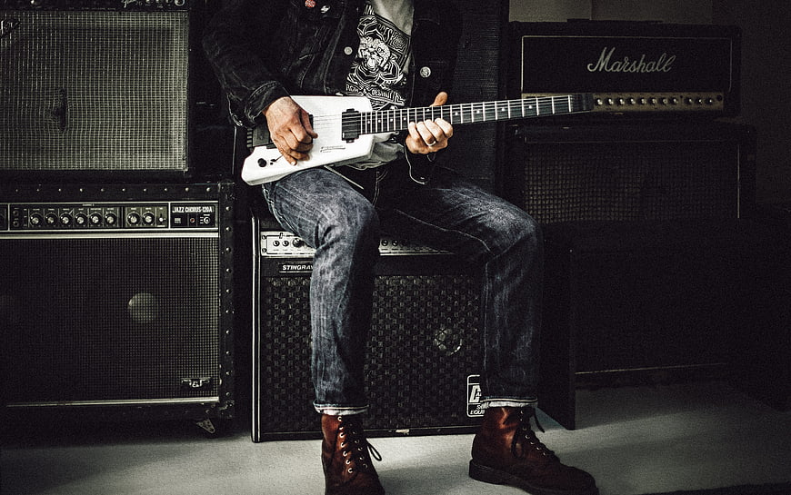 Rock musician playing white electric guitar with amplifiers