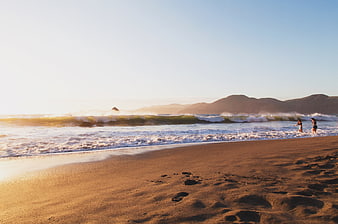 Golden Hour Beach Scene with Waves and Distant Figures