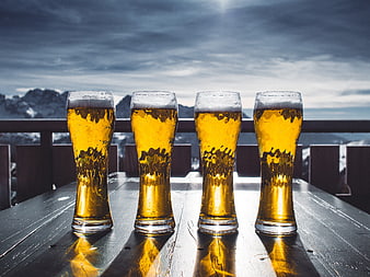 Four glasses of beer on a wooden table with snowy mountains