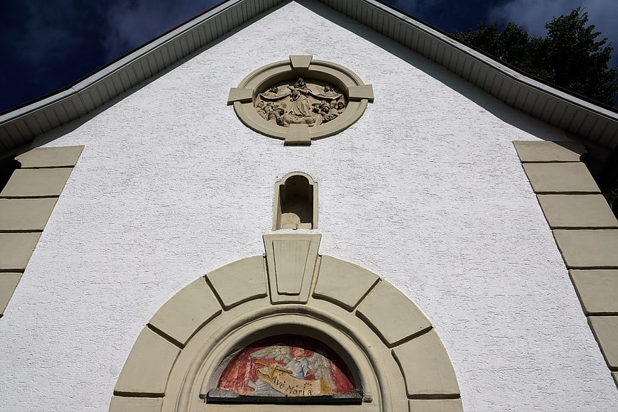 White chapel facade with religious sculpture and Ave Maria painting