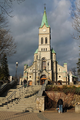 Grand stone church with green spire and dramatic sky