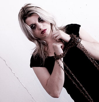 Blonde woman with chains and dark makeup against white wall