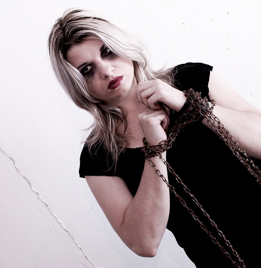 Blonde woman with chains and dark makeup against white wall