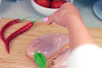 Hand seasoning raw chicken breast with spices on wooden board