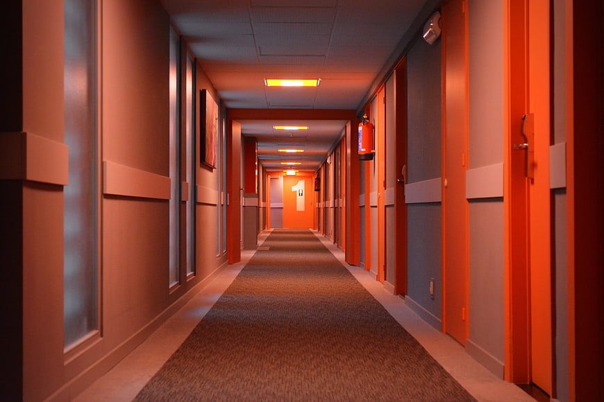 Empty Hotel Hallway With Orange Doors And Carpeted Floor