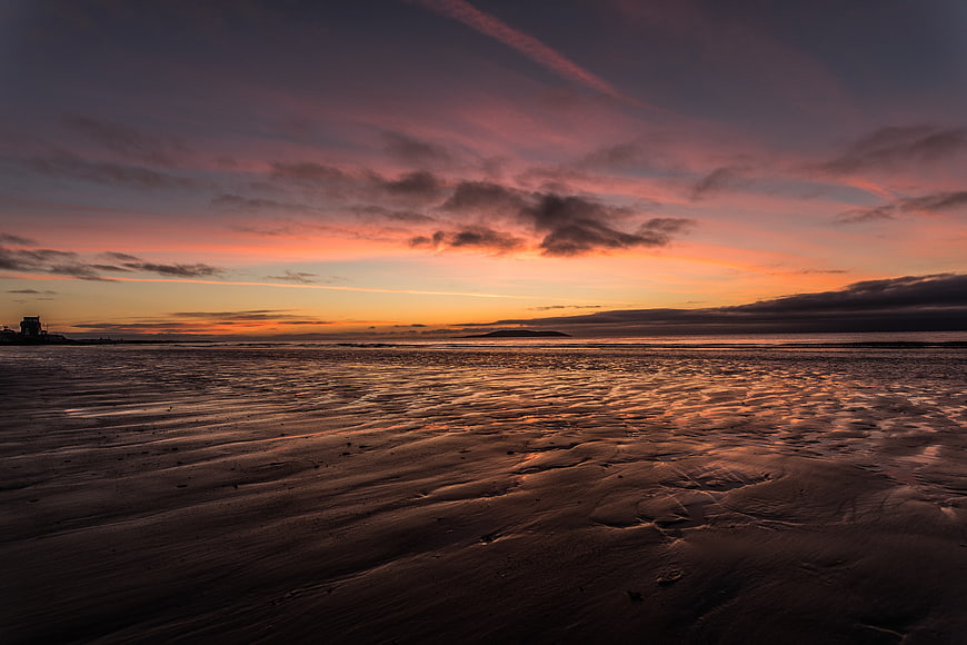 Dramatic Sunset Over Wet Sandy Beach with Ripples