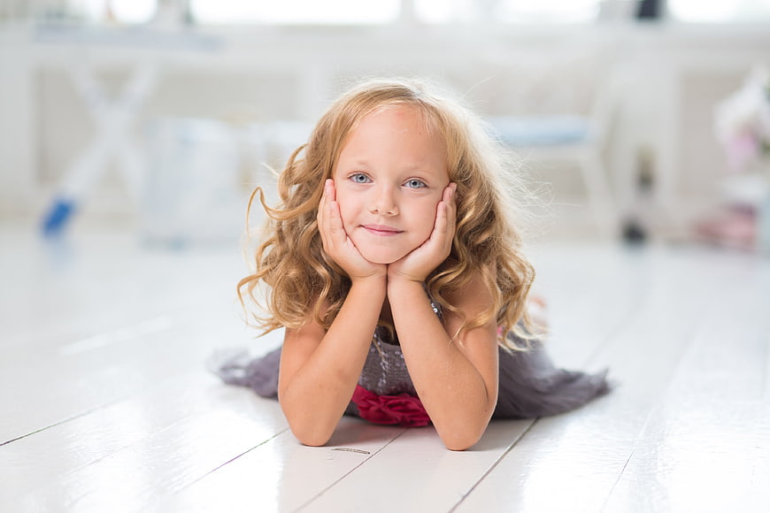 Cute little girl lying on white floor with hands on cheeks
