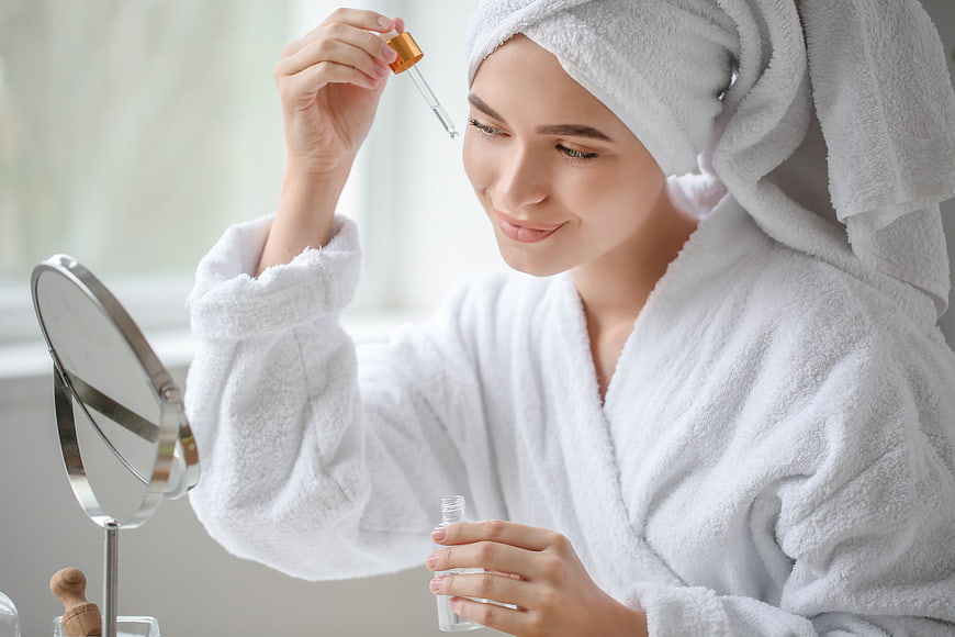 Woman applying serum with dropper in white bathrobe