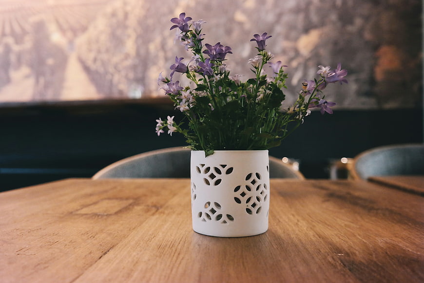 Purple flowers in white ceramic vase on wooden table