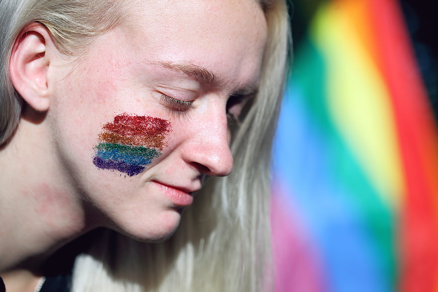 Close-up of woman with rainbow glitter face paint and pride flag background