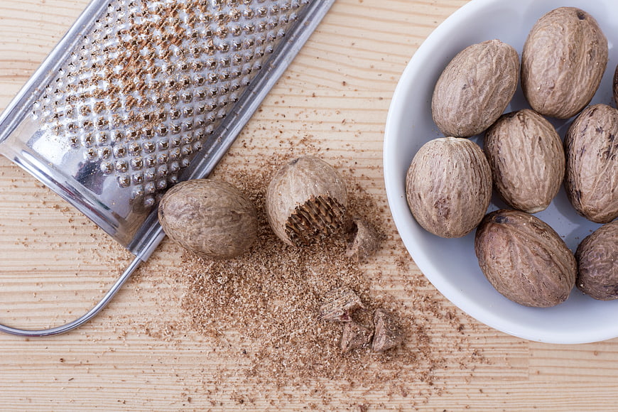 Whole Nutmegs and Grated Spice on Wooden Surface