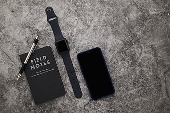 Flat lay of smartwatch, smartphone, and Field Notes notebook on concrete