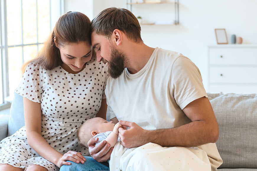 Young parents holding newborn baby on sofa