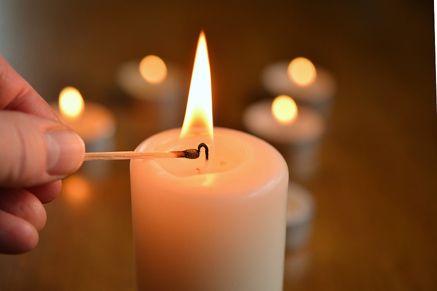 Hand lighting a white candle with a matchstick