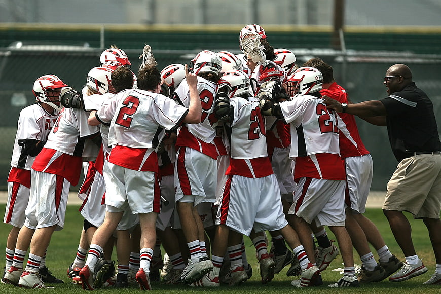 Lacrosse team huddle celebrating with coach on field