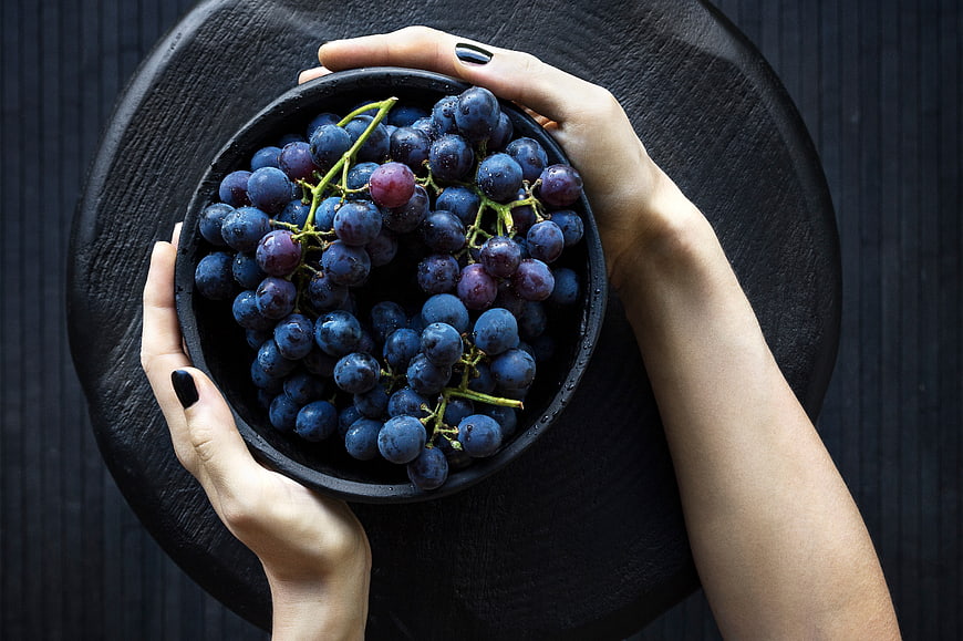 Top view of hands holding a bowl of fresh blue grapes