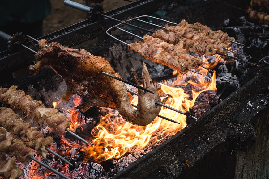 Whole roasted duck and skewers grilling over charcoal fire