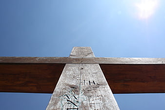 Low angle view of weathered wooden cross against blue sky