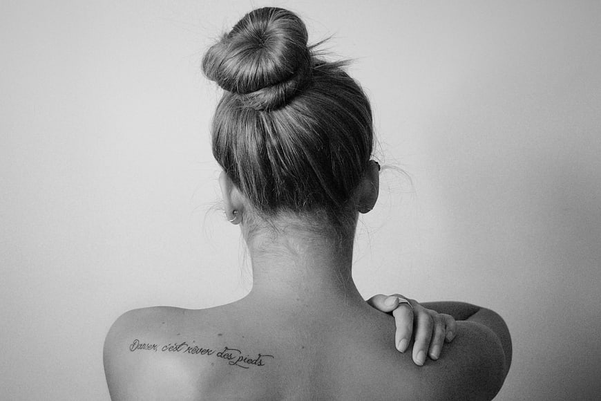 Black and white portrait of a woman's back with a French script tattoo