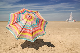 Colorful striped beach umbrella on sandy shore with sailboat