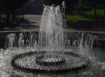 Sparkling water fountain in a sunny park with benches