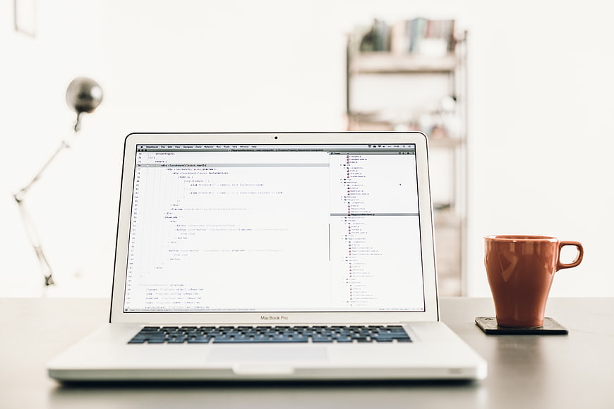 Laptop with code on screen and coffee mug on desk