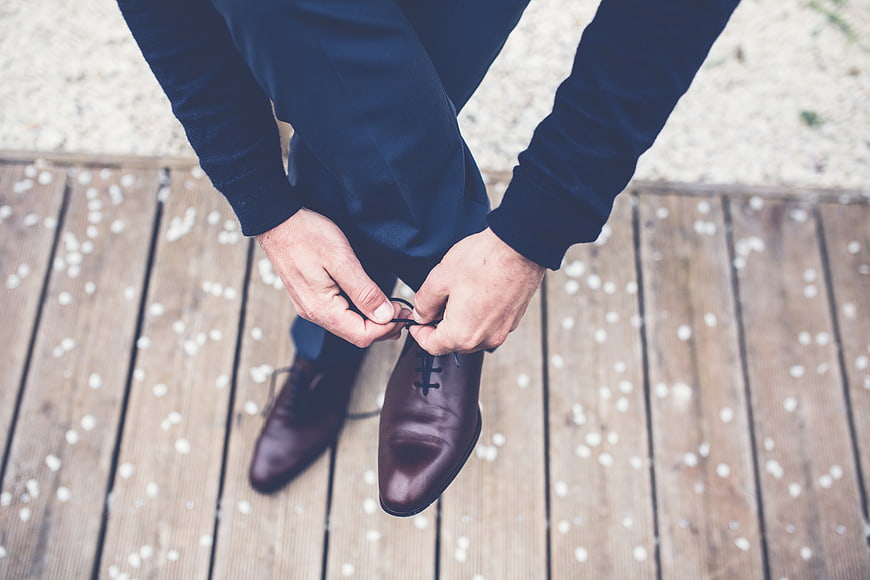 Man tying brown leather dress shoes on wooden deck