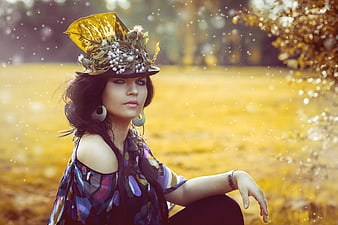 Young woman in ornate floral hat and colorful top in autumn field