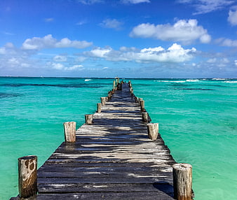 Weathered wooden pier extending into turquoise ocean water under a bright blue sky