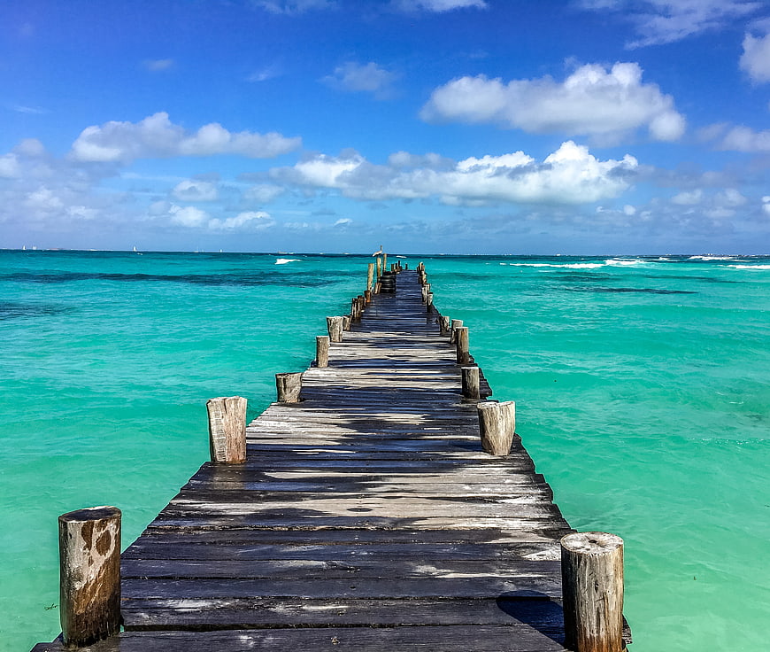 Weathered wooden pier extending into turquoise ocean water under a bright blue sky