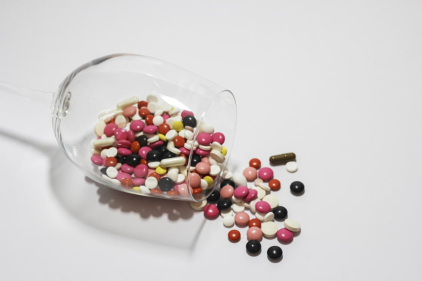 Colorful pills spilling from a tipped wine glass on a white background
