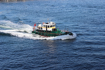 Green and white harbor tugboat moving through blue sea water