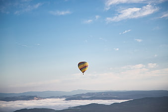 Colorful hot air balloon flying over sea of clouds and mountains