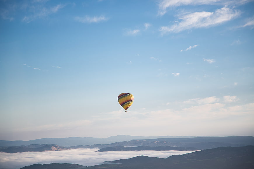 Colorful hot air balloon flying over sea of clouds and mountains