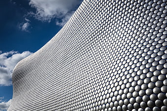 Modern curved building facade with silver scales against blue sky