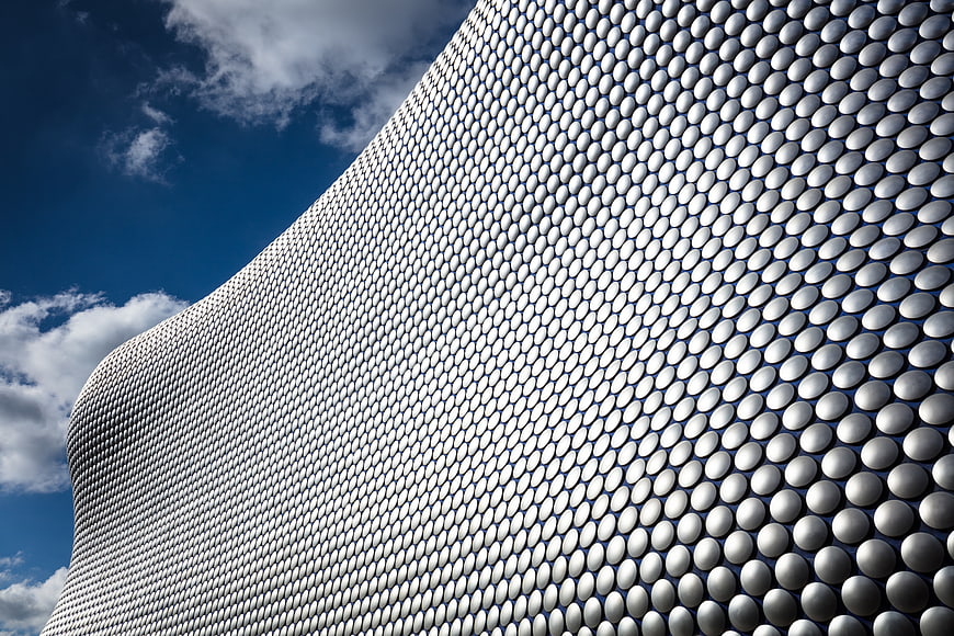 Modern curved building facade with silver scales against blue sky