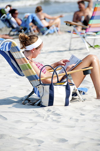 Woman reading newspaper on beach chair with tote bag